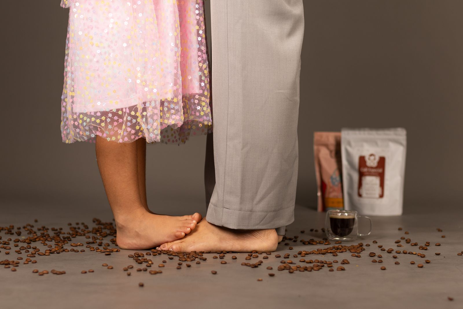 Isadora sobre os pés da mãe, entre grãos de café e pacotes Adora Cafés